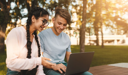 Friendly international college classmates preparing for lectures outdoors, sitting in park or college campus with laptop. Break between classes concept