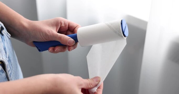 Woman removing sticky tape from lint roller indoors, closeup