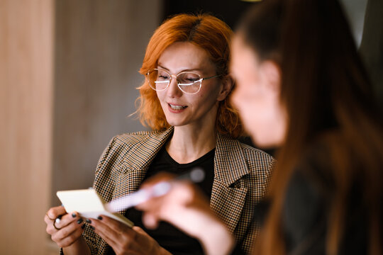 Meeting between two professionals in a modern office setting as they discuss ideas on a notepad in the afternoon