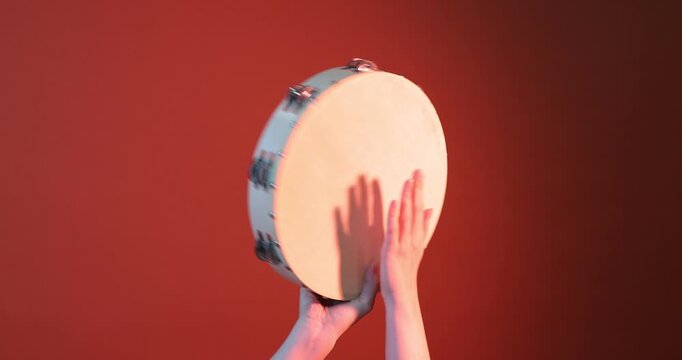 Woman playing tambourine on color background, closeup
