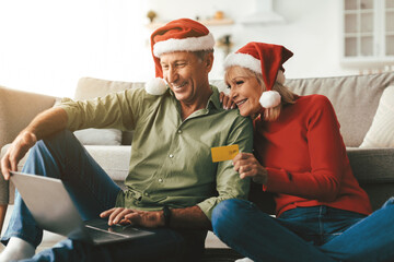 Mature Couple Shopping Online Buying Christmas Gifts Using Credit Card And Laptop Sitting At Home. Happy Customers Wearing Santa Hats Purchasing Presents During Winter Holiday Sales Season