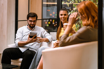 People enjoying a casual gathering in a modern indoor setting while engaging with technology and having beverages in the afternoon light
