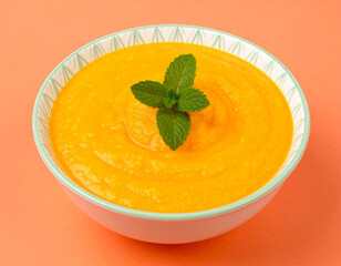 A bowl of soup with a green leaf on top. The soup is orange and has a thick consistency