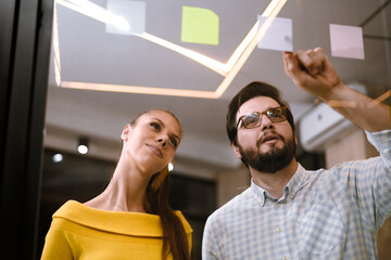 Team members engaging in a creative brainstorming session in a modern office setting with colorful sticky notes on a glass board