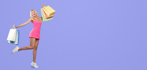 Huge Sales Concept. Full body length shot of excited stylish blonde lady walking and posing with raised leg and arms holding shopper bags from mall, happy about purchase or gifts, blue studio wall