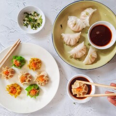 Assorted Asian Dumplings and Shumai with Dipping Sauces on White Background