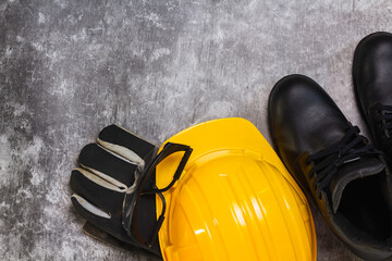 Close-up top view of protective equipment on a construction site: yellow hard hat, goggles and leather gloves lying on the floor.