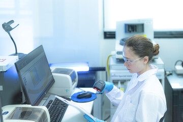 A diligent female scientist in a high-tech lab cross-references a printed report with data graphs on her computer, meticulously verifying experimental results for a research study.