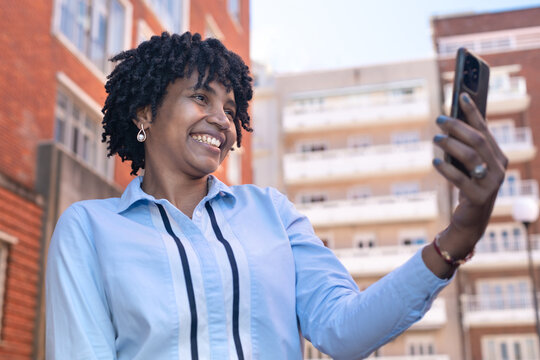 Smiling black woman happily taking selfie or having video call in urban setting - Powered by Adobe