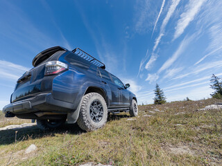 Off-road SUV parked on grassy ridge under vibrant blue sky with streaked clouds in Dolly Sods, West Virginia