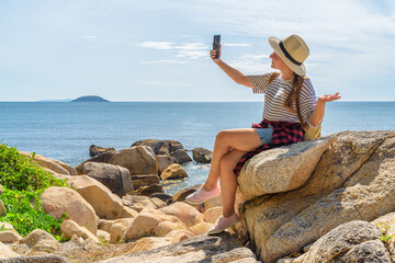 Woman is sitting on a rock and using video call