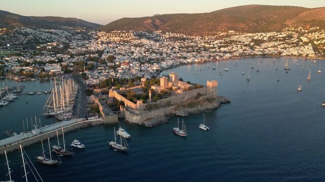Bodrum, Turkey: Aerial drone footage of sunset over castle in Bodrum. Taken with rotating motion, showing the yachts docking in marina, city landscape, and mountain in the background