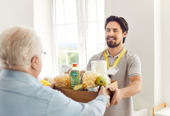 Happy volunteer guy giving a box of groceries to an elderly man, close-up. Help for pensioners, social initiative, food distribution. Concept donation bag, canned food, humanitarian aid