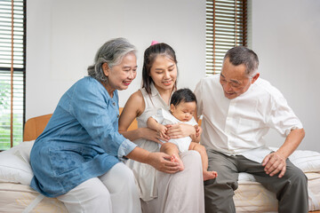 Asian Family Sitting Together, Playing with a Baby, Grandparents and Mother Happily Bonding with Their Newborn Infant at Home, Multi-Generational Asian Family Caring for and Admiring the New Baby