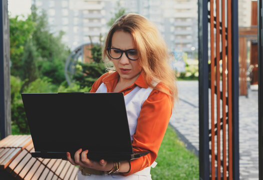 A young business woman focused on her laptop while sitting outdoors in a city park, embracing the freelancer lifestyle with joy and style.