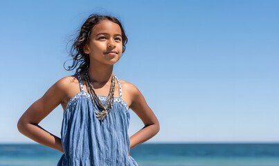 a cute Indigenous Australian girl aged 11 years old, standing with her hands on her hips looking proud. She's standing on a beach on a beautiful sunny day