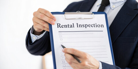 Rental inspection checklist held by person in suit for rent property generation process with pen on clipboard