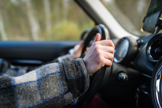 Closeup of woman hands holding steering wheel driving vehicle. Female traveling by car, using navigation app on smartphone, observing speed limit, drives through the autumn countryside landscape