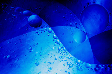 Macro photography of floating oil bubbles in blue fluid forming abstract wave patterns.