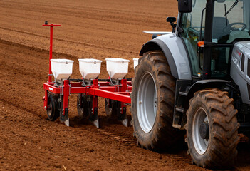 a modern tractor equipped with a seed planting machine operating in a freshly plowed field. 