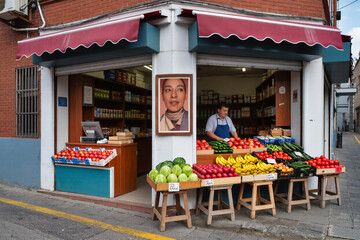 8K ultra-realistic photo of small corner grocery shop with fresh fruits and vegetables displayed outside and owner standing at counter, natural daylight