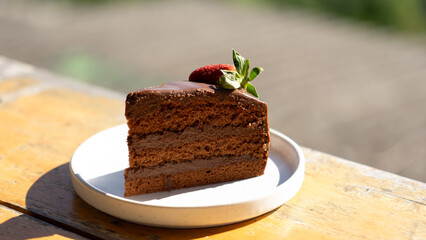 Chocolate Cake Delight: A delectable slice of rich chocolate cake, adorned with a fresh strawberry and a sprig of mint, sits invitingly on a pristine white plate, a tempting treat for dessert lovers.