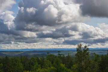 sweeping landscape reveals lush green forests beneath vast sky filled with large, fluffy clouds. scene captures tranquility nature, inviting calm and reflection.