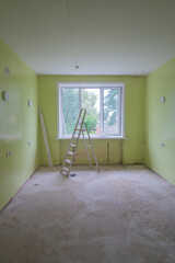 room is being renovated, featuring bright green walls and window that lets in natural light. ladder stands in center, awaiting further work on unfinished floor. close up.