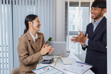 Two colleagues celebrate a successful discussion with cheerful expressions and clapping. Their positive interaction reflects teamwork, motivation, and satisfaction after reviewing reports.