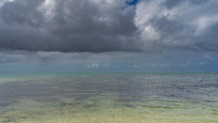 Obraz premium Beautiful seascape under a cloudy sky. Turquoise ocean, ripples on the surface of the water, foam waves on the horizon. There are dark clouds in the blue sky. Mauritius.
