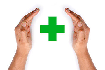 Green medical cross covered by hands on white background.