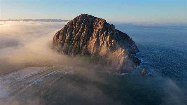 Stunning aerial views of a magnificent Morro Bay Rock island completely surrounded by a thick layer of fog, capturing the serene and captivating beauty of nature in all its glory, Pacific Ocean, USA