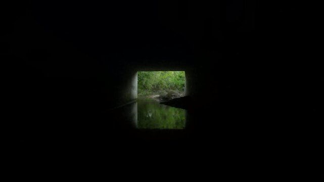 Creek flowing through concrete culvert toward daylight &mdash; light at the end of the tunnel