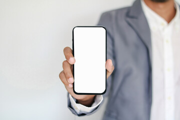 Hand holding smartphone with blank screen for mockup at modern workspace. Laptop, tablet, and notebook on desk. Concept of mobile app, digital business, and technology.