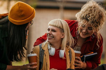 Young women friends laughing enjoying coffee outdoors