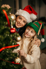 Mother and daughter decorating christmas tree wearing festive hats