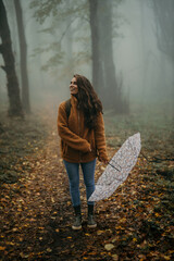 Woman smiling in autumn forest with fog holding umbrella