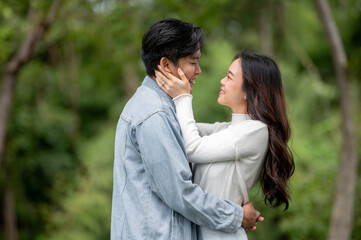 Obraz premium Young asian couple hugging as woman holding or touching a man's face while standing outdoors in park
