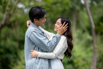 Naklejka premium Young asian couple hugging as a man holding or touching woman's face while standing outdoors in park
