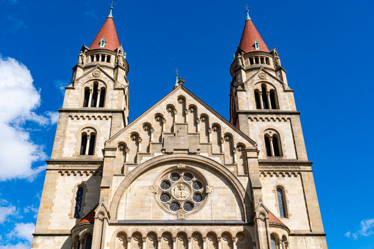 Front view of a historic Romanesque church with twin towers and red roofs under bright blue sky, architectural detail of a European cathedral facade.