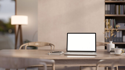 Blank screen laptop with coffee cup aside pencil on notebook and vase on wooden table in living room
