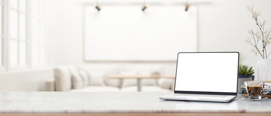 White screen laptop and coffee on marble table across sofa and blank frame on wall with ceiling lamp