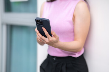 Close up of a woman's hands holding and using smartphone while standing or leaning against the wall.