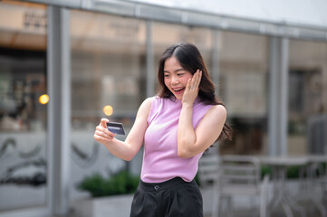 Young asian woman looking at credit card in surprised while standing or walking in front of a cafe