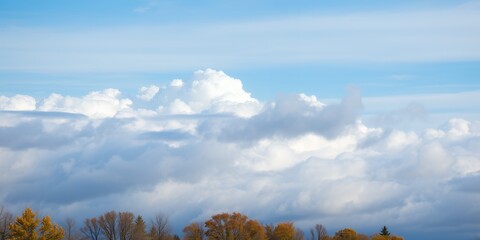 Cumulus clouds fill a bright blue sky above autumn trees with yellow and orange foliage
