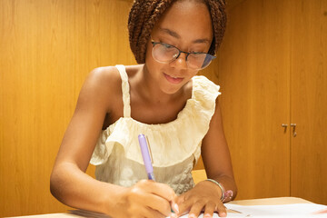 Smiling girl student in glasses writing notes on paper, learning and studying