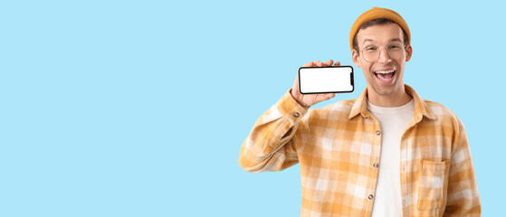 Happy young man with blank mobile phone on blue background