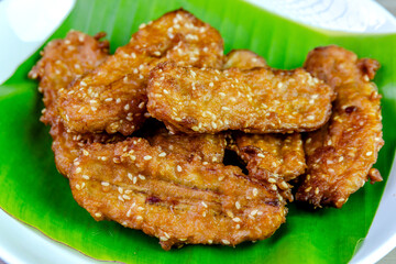 Crispy Thai fried bananas with sesame seeds served on a banana leaf in a white plate, Fried bananas is a traditional Asian snack with sweet, crunchy texture. Top view close-up shot