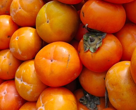selective image of fresh ripe persimmon fruit (Diospyros kaki) displayed together at a local market for sale. ideal for fruit background and vegetarian diet or natural food design theme