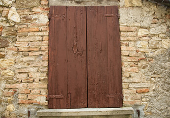 A weathered brown wooden shutter on a rustic stone and brick wall at Serravalle Castle, Bologna, Italy.